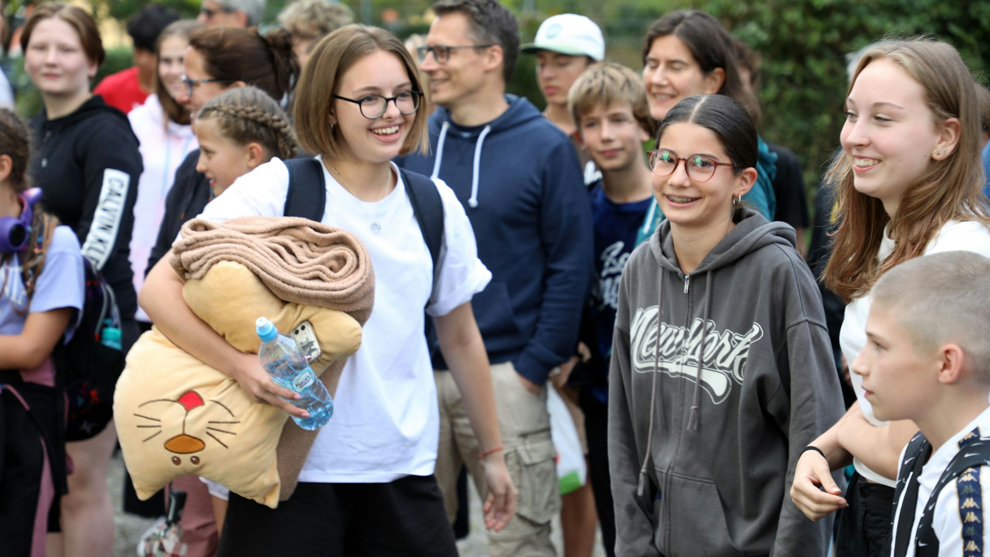 Schülerinnen und Schüler, Lehrerinnen und Lehrer und Eltern und andere Menschen stehen mit Fahnen von Ukraine, Deutschland, Butscha und Bergisch Gladbach auf dem Schulhof der Integrierten Gesamtschule Paffrath und jubeln.