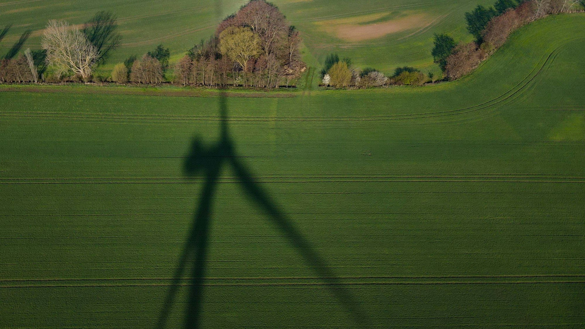 Das Foto zeigt den Schatten einer Windenergieanlage auf einem Feld.