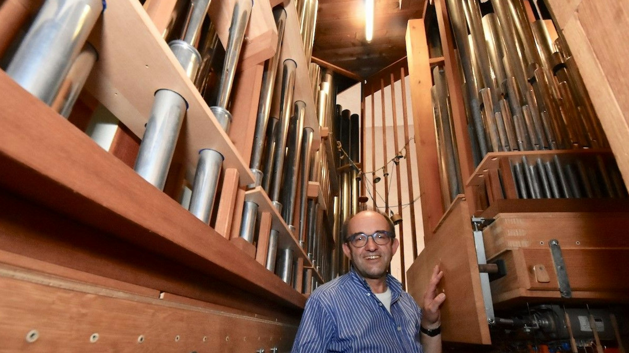 Ein Mann im blau-weiß gestreiften Hemd steht zwischen den Pfeifen einer Orgel.