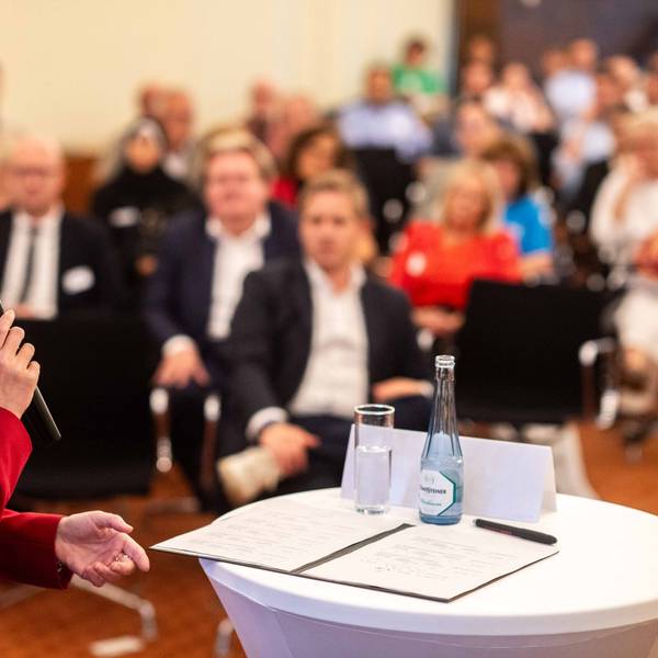 Das Bild zeigt Ministerin Ina Scharrenbach mit einem Mikrofon in der Hand, wie sie zum Publikum spricht.