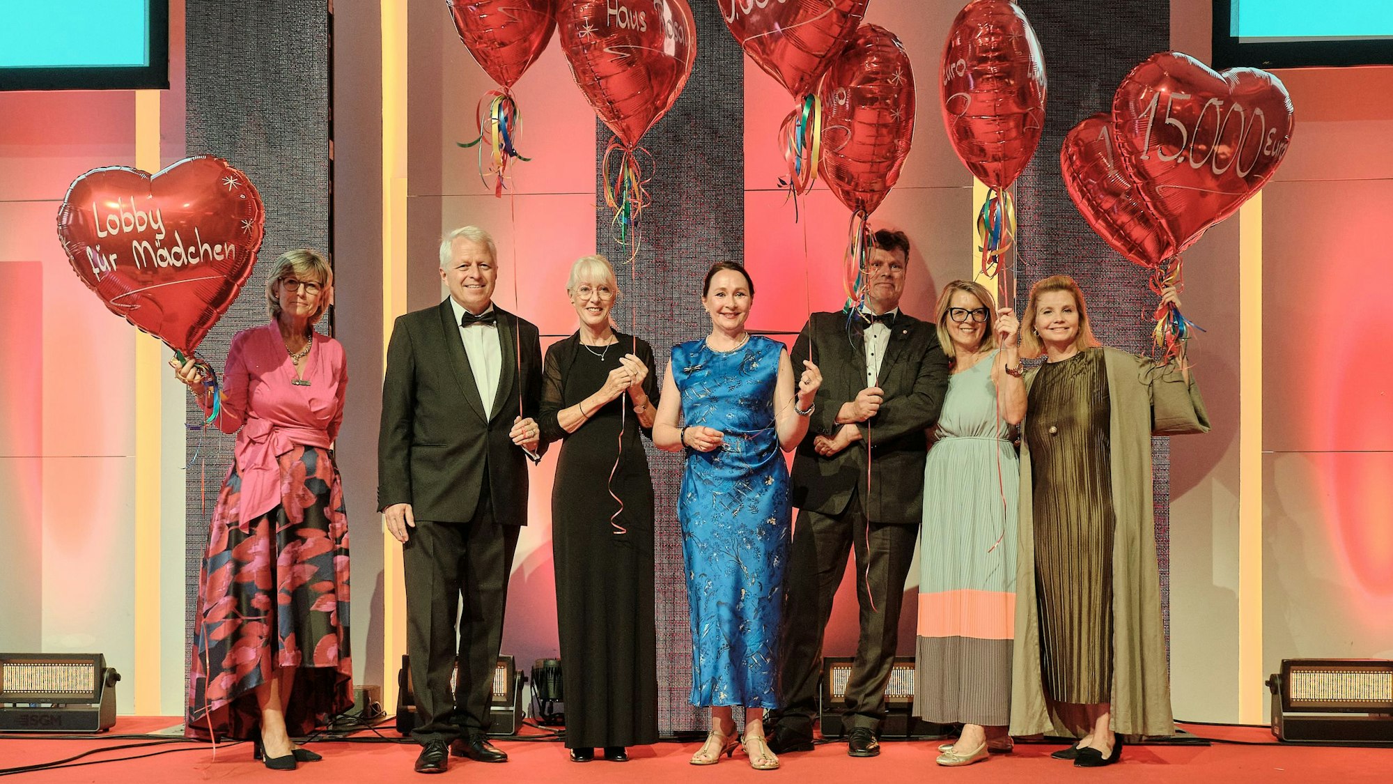 Die Paten stehen auf der Bühne und haben Luftballons in Herzform in der Hand.