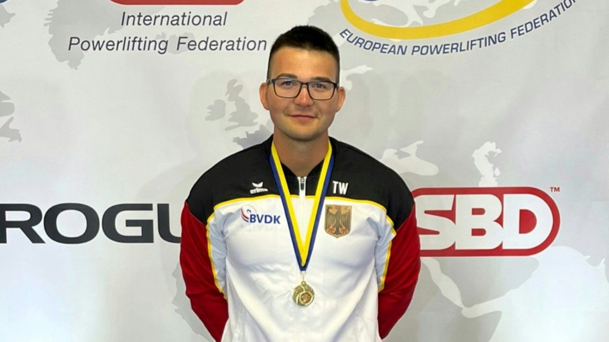 Ein Mann in Sportkleidung trägt eine Medaille um den Hals.