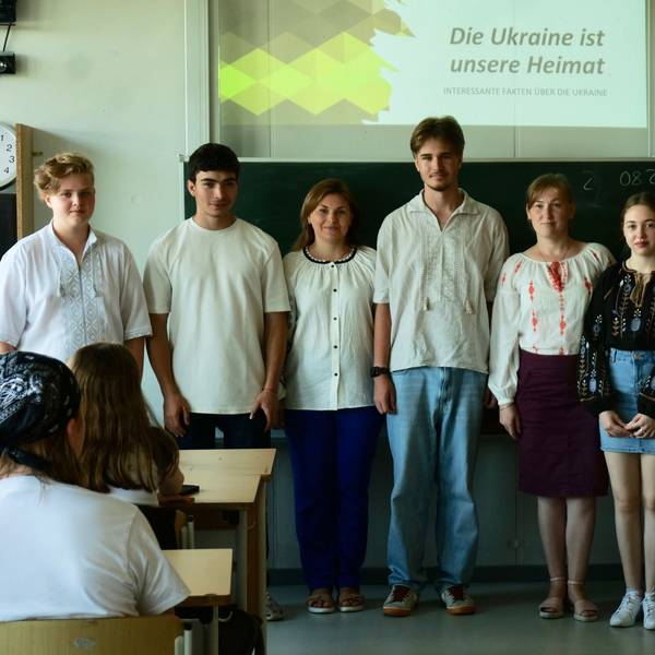 Eine Gruppe von Schülern und Lehrern steht vor einer Tafel in einem Klassenzimmer.