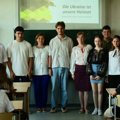 Eine Gruppe von Schülern und Lehrern steht vor einer Tafel in einem Klassenzimmer.
