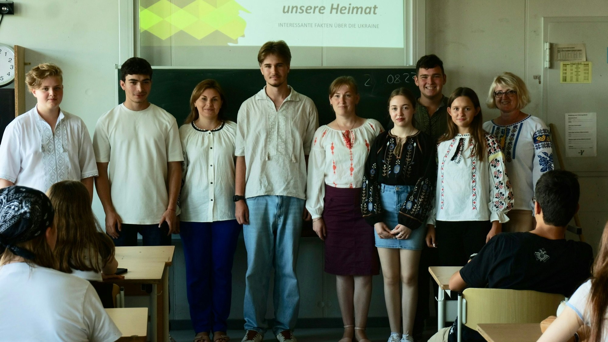 Eine Gruppe von Schülern und Lehrern steht vor einer Tafel in einem Klassenzimmer.