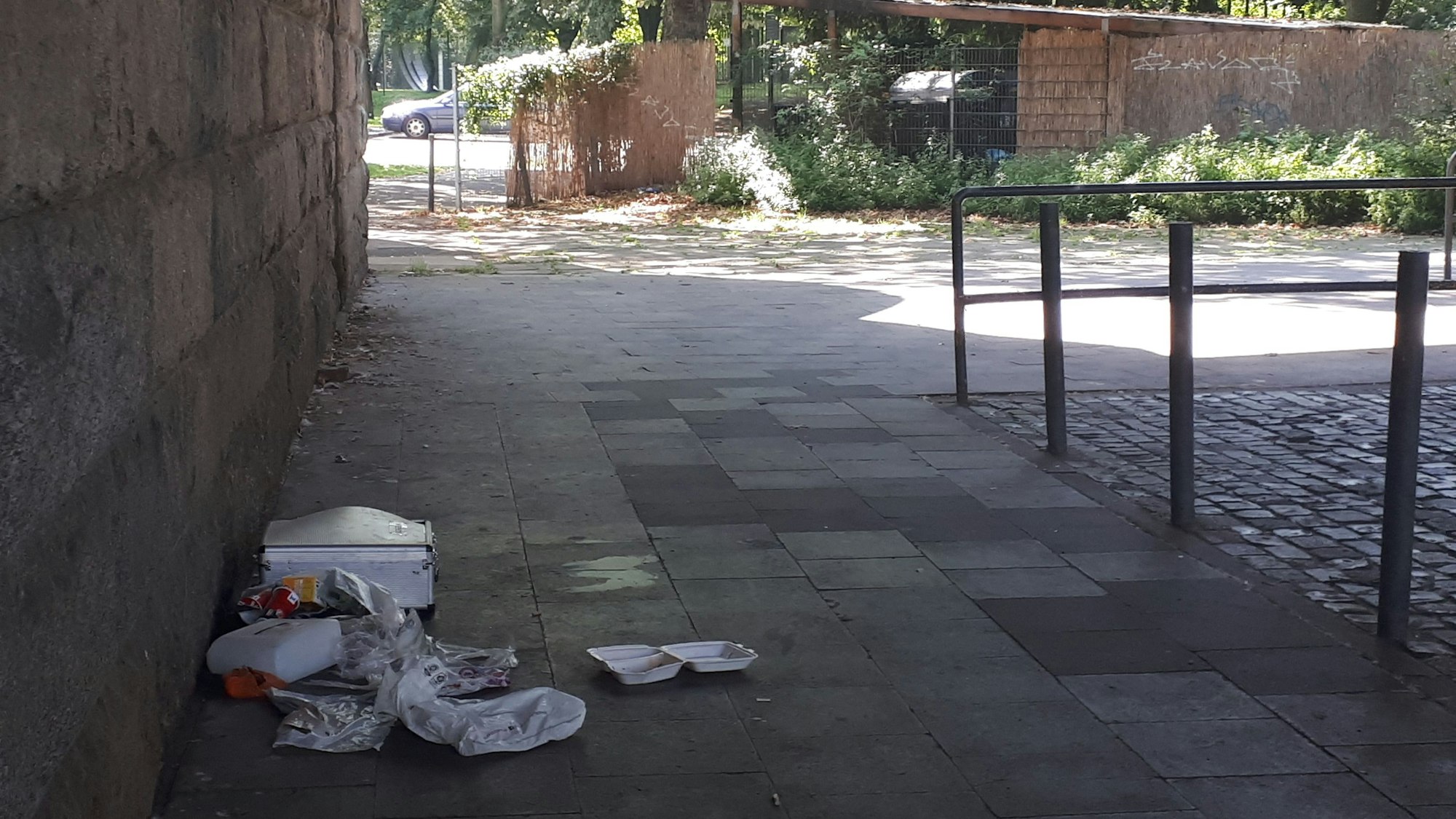 Plastiktüten und leere Essensverpackungen liegen auf dem Boden neben einem Pfeiler der Zoobrücke.