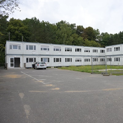 Man sieht zwei über Eck gebaute Riegel von grauen Containerbauten.
