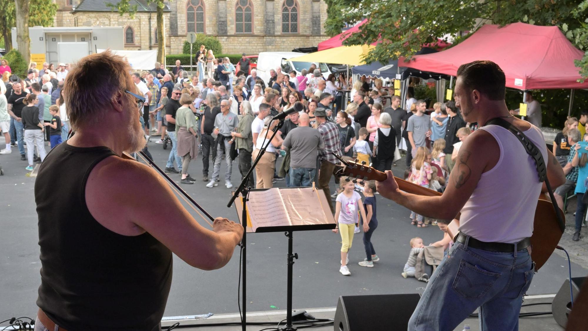 Zwei Musiker stehen auf der Bühne, im Hintergrund ist das Publikum zu sehen.