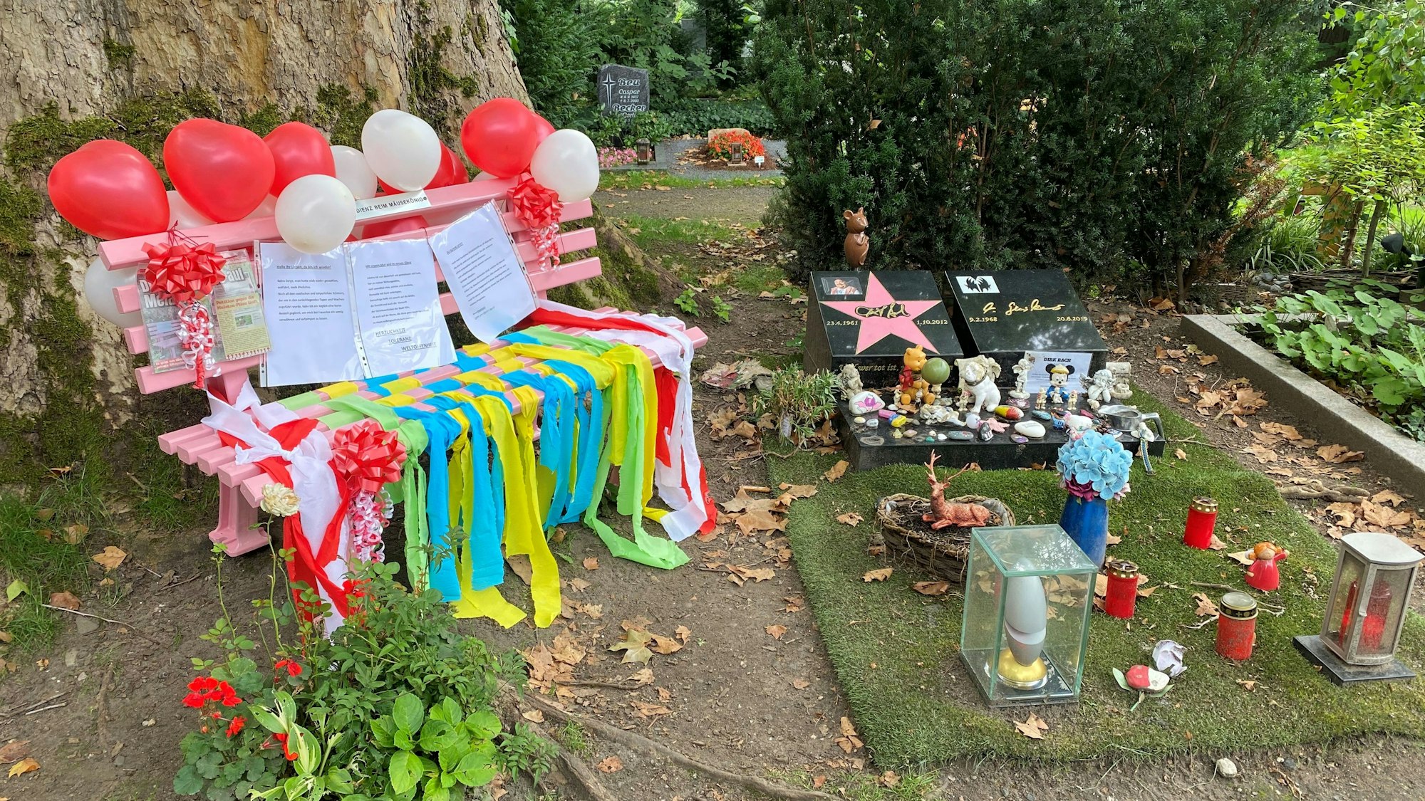 Eine rosafarbene Bank mit Ballons und Bändern neben einem Grab.