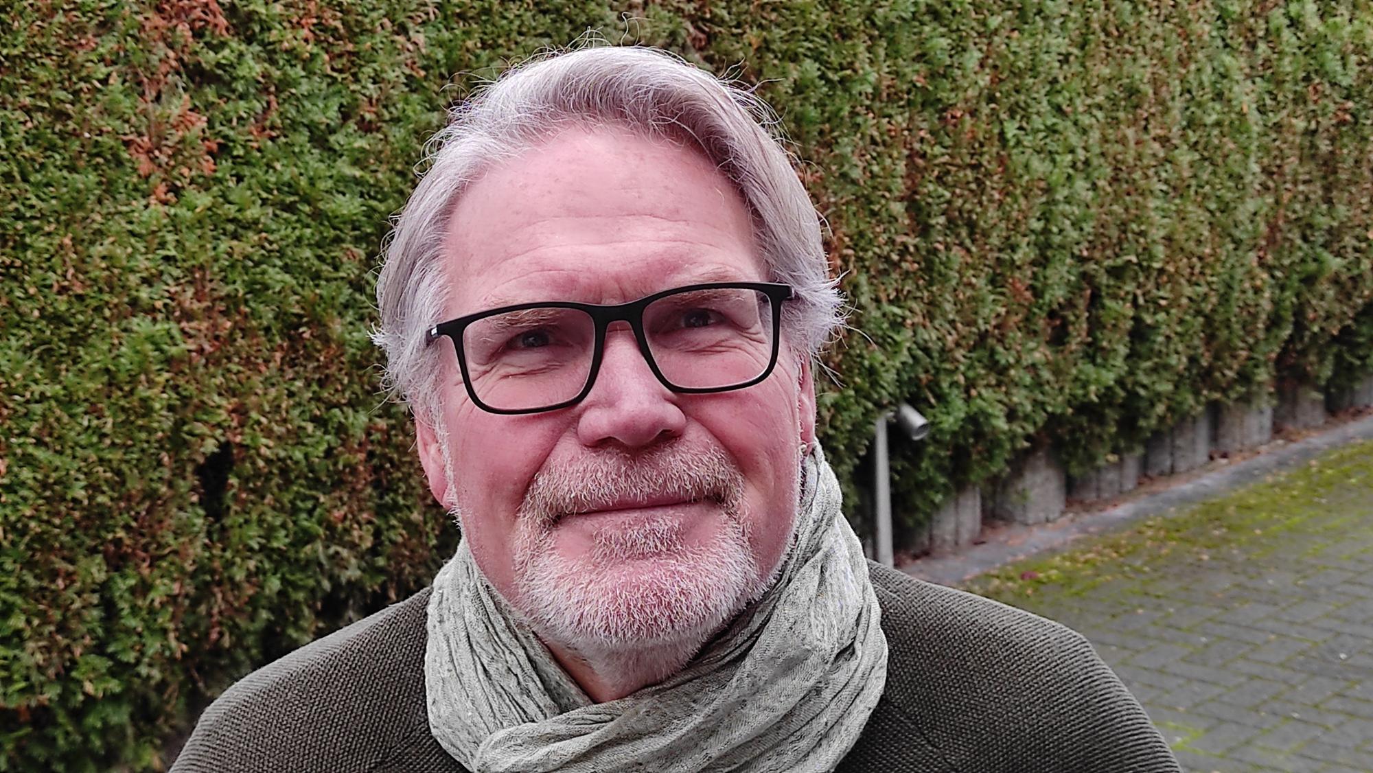 Hans Werner Klinkhammels, der Seniorenbeauftragte der Stadt Niederkassel und Vorsitzende des Niederkasseler Seniorenbeirats, steht vor einer grünen Hecke.