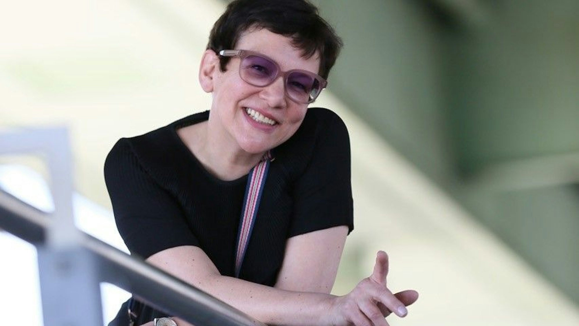 Claudia Malzkorn, eine Frau mit kurzen, schwarzen Haaren und Sonnenbrille steht auf einer Treppe und hält den Zeigefinger in die Höhe