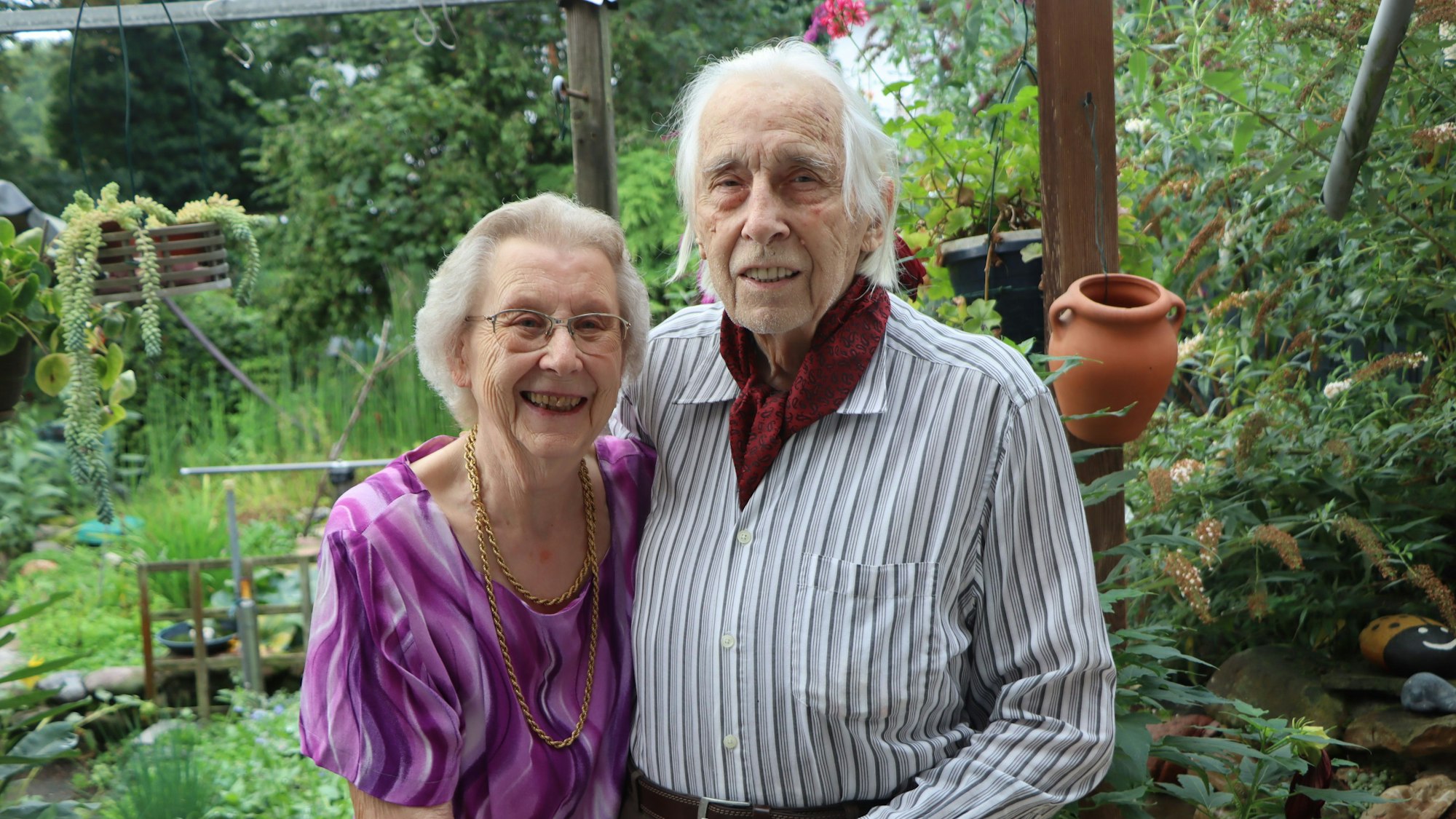 Ein hoch betagtes Paar steht in einem Garten und hält sich an den Händen.
