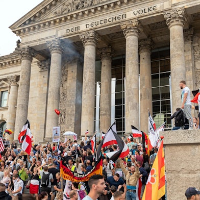 Berlin: Teilnehmer einer Kundgebung gegen die Corona-Maßnahmen stehen auf den Stufen zum Reichstagsgebäude, zahlreiche Reichsflaggen sind zu sehen.