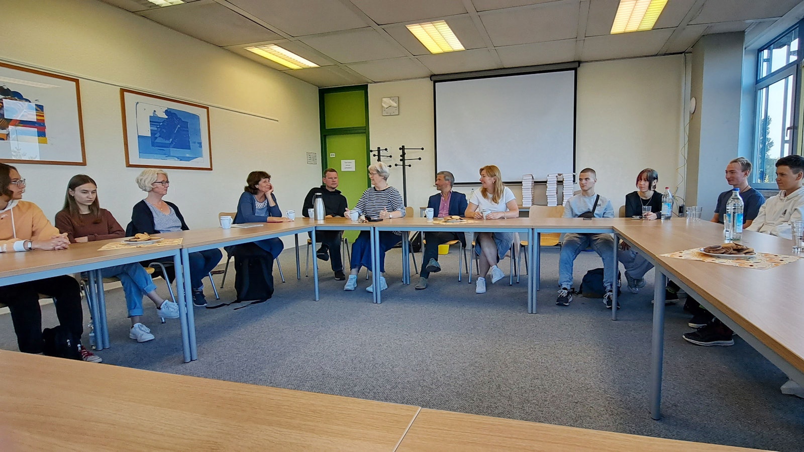 Schülerinnen und Schülern aus Butscha sitzen mit Lehrerinnen und Lehrern an einem Tisch.