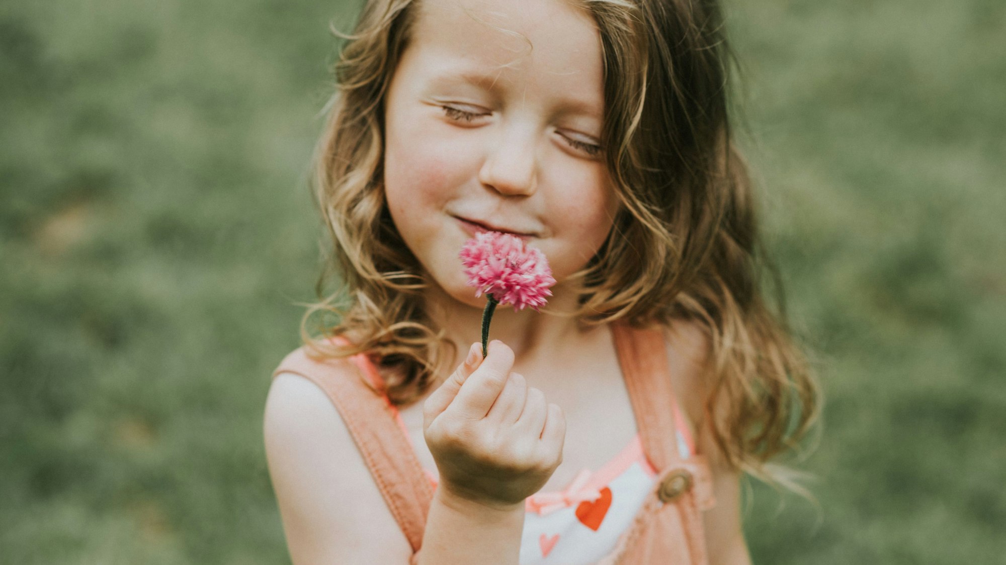 Ein kleines Mädchen hält eine Kornblume vor den Mund und hat die Augen geschlossen, als Geste der Dankbarkeit.