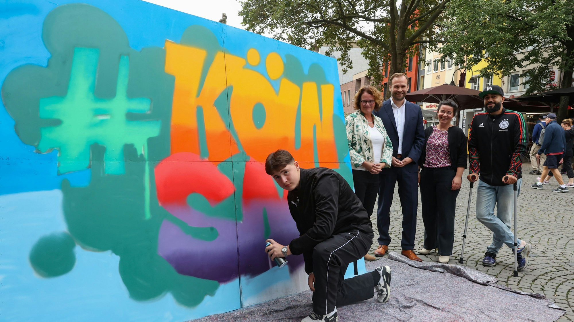 Ein Jugendlicher sprayt den Tag #kölnsafe auf eine mobile Wand
