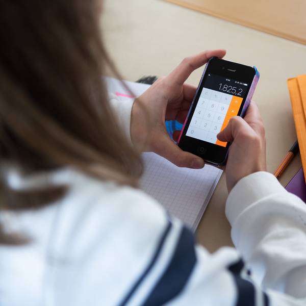 Ein Mädchen hält ein Smartphone im Klassenraum ein Smartphone in der Hand.