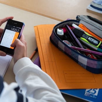 Ein Mädchen hält ein Smartphone im Klassenraum ein Smartphone in der Hand.