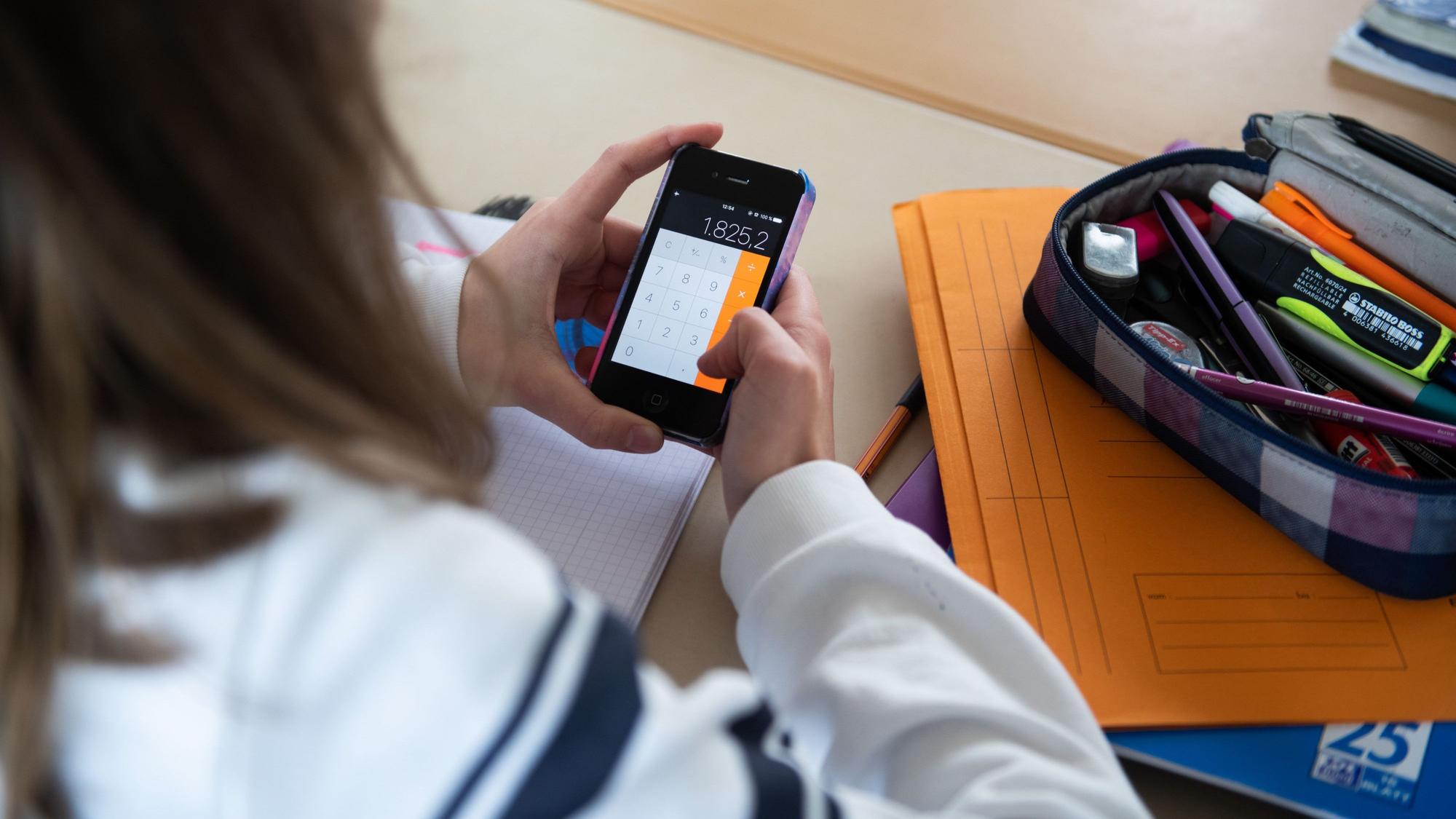 Ein Mädchen hält ein Smartphone im Klassenraum ein Smartphone in der Hand.
