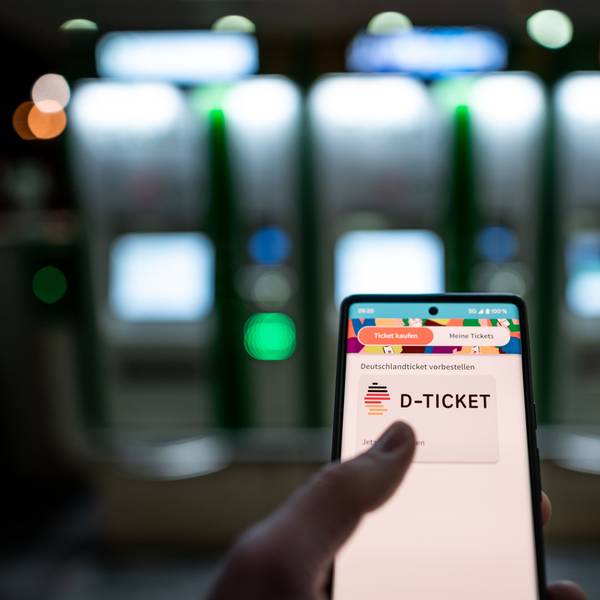Ein Mann hält ein Mobiltelefon, auf dem das „D-Ticket“ gekauft werden kann, vor dem Ticketautomaten am Hauptbahnhof Essen in der Hand.