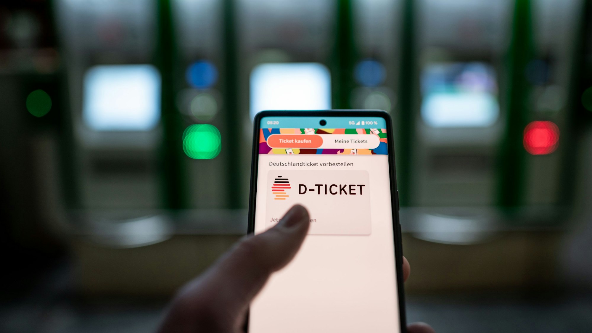 Ein Mann hält ein Mobiltelefon, auf dem das „D-Ticket“ gekauft werden kann, vor dem Ticketautomaten am Hauptbahnhof Essen in der Hand.