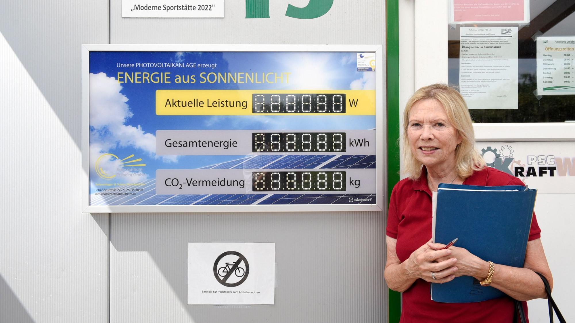 Eine Frau steht neben dem Zähler einer Photovoltaikanlage.
