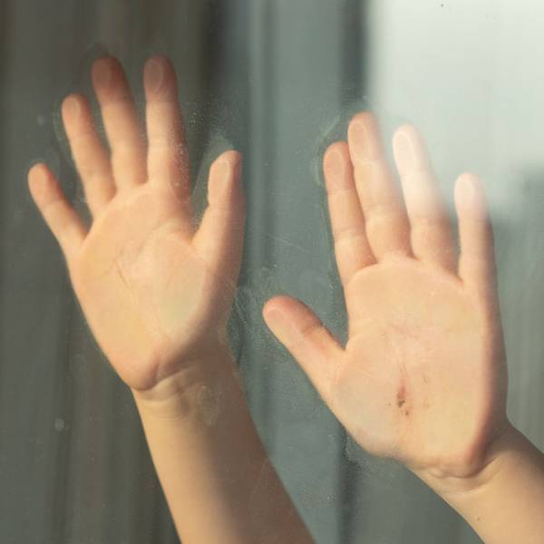 Kinderhände halten sich an einer Glasscheibe fest.