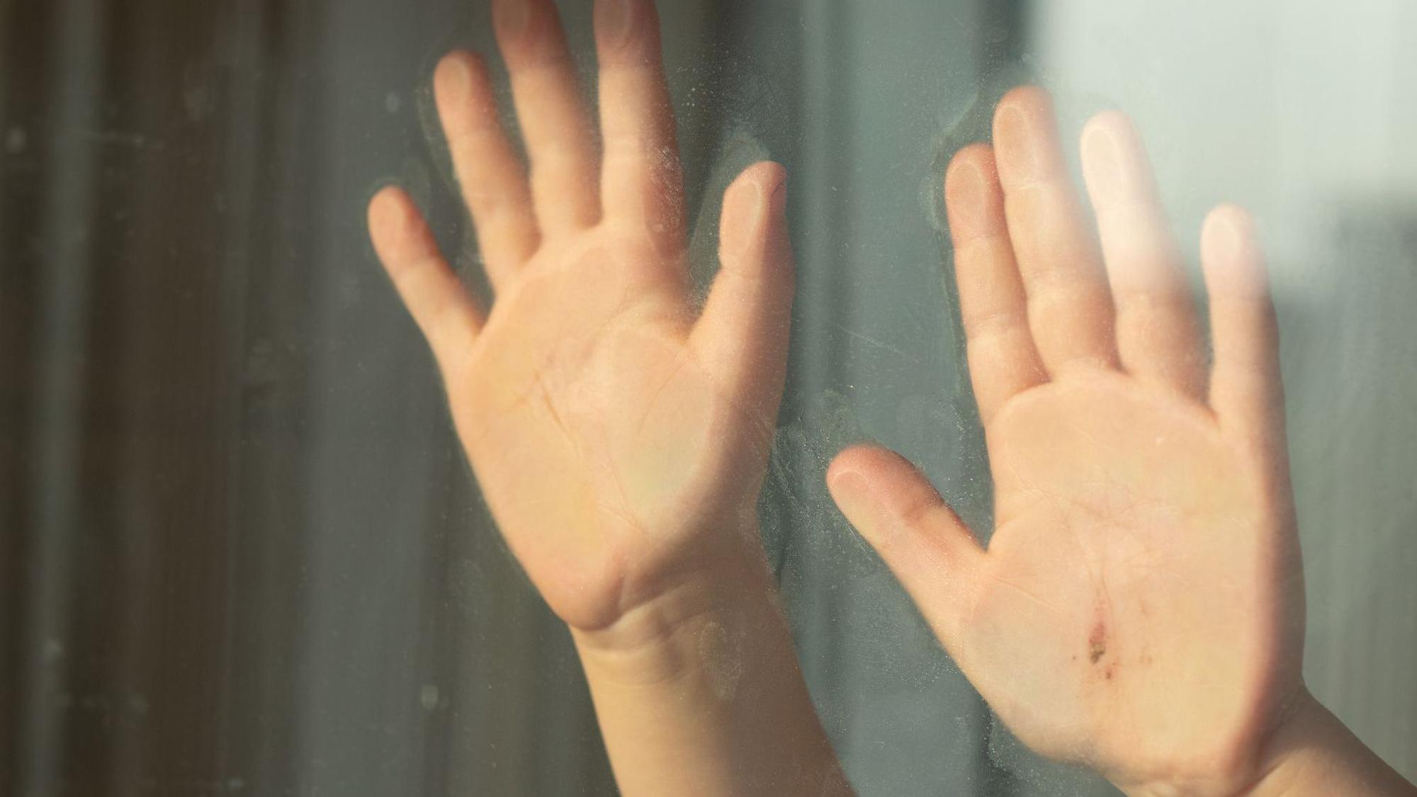 Kinderhände halten sich an einer Glasscheibe fest.