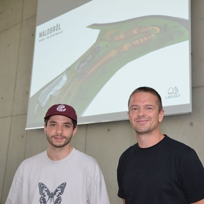 Daniel Schreitmüller (links) und Tobias Hunger von der Landskate GmbH in Köln planen den Rollsport an der Klus in der Ortschaft Niederhof. Jetzt haben sie in Waldbröls Bürgerdorf am Alsberg ihre Pläne in 3D vorgestellt. Sie stehen vor einer Leinwand.