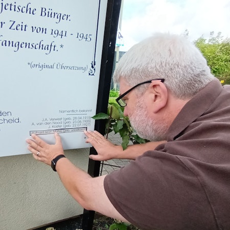 Ein Mann klebt einen Namen auf eine Gedenktafel.