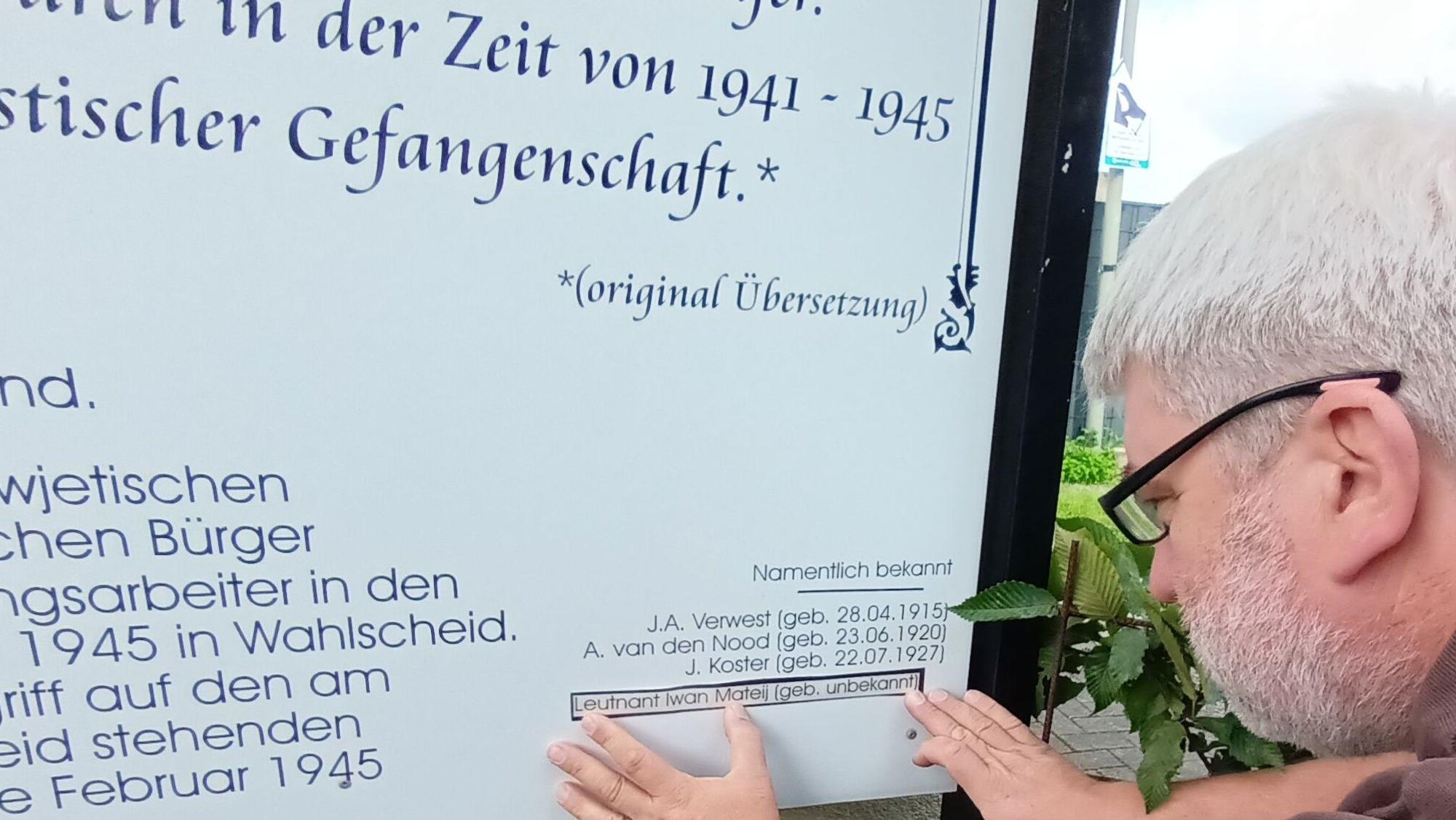 Ein Mann klebt einen Namen auf eine Gedenktafel.