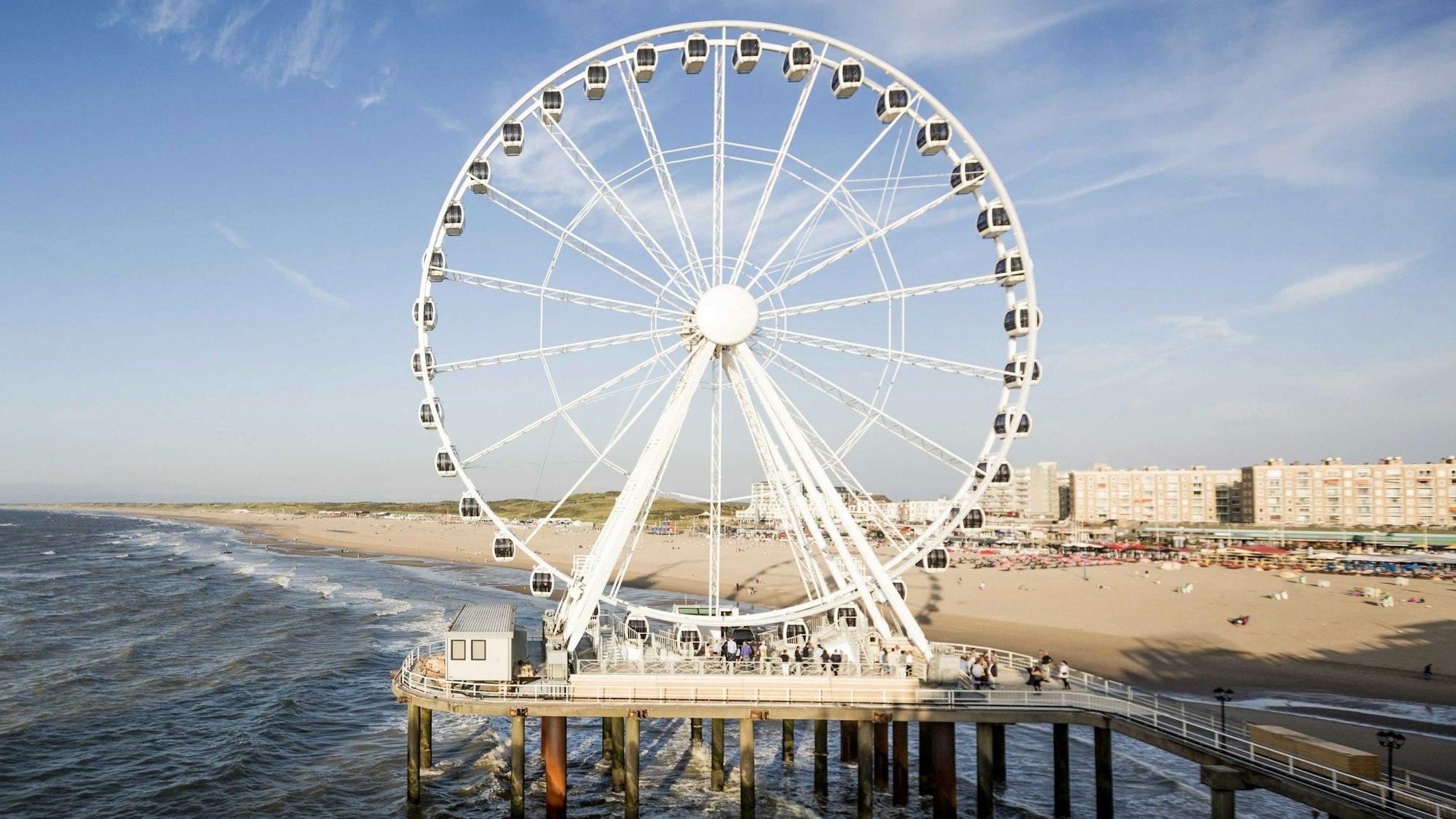 Der Nordseestrand im niederländischen Scheveningen bei Den Haaf mit seinem Riesenrad auf einem Pier. Im Hintergrund sind Urlauber am Strand zu sehen.