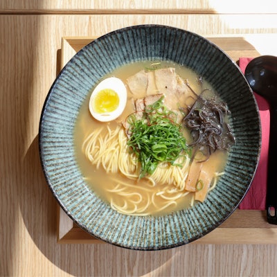 Wir sehen eine Suppenschüssel von oben, daneben Löffel und Stäbchen.