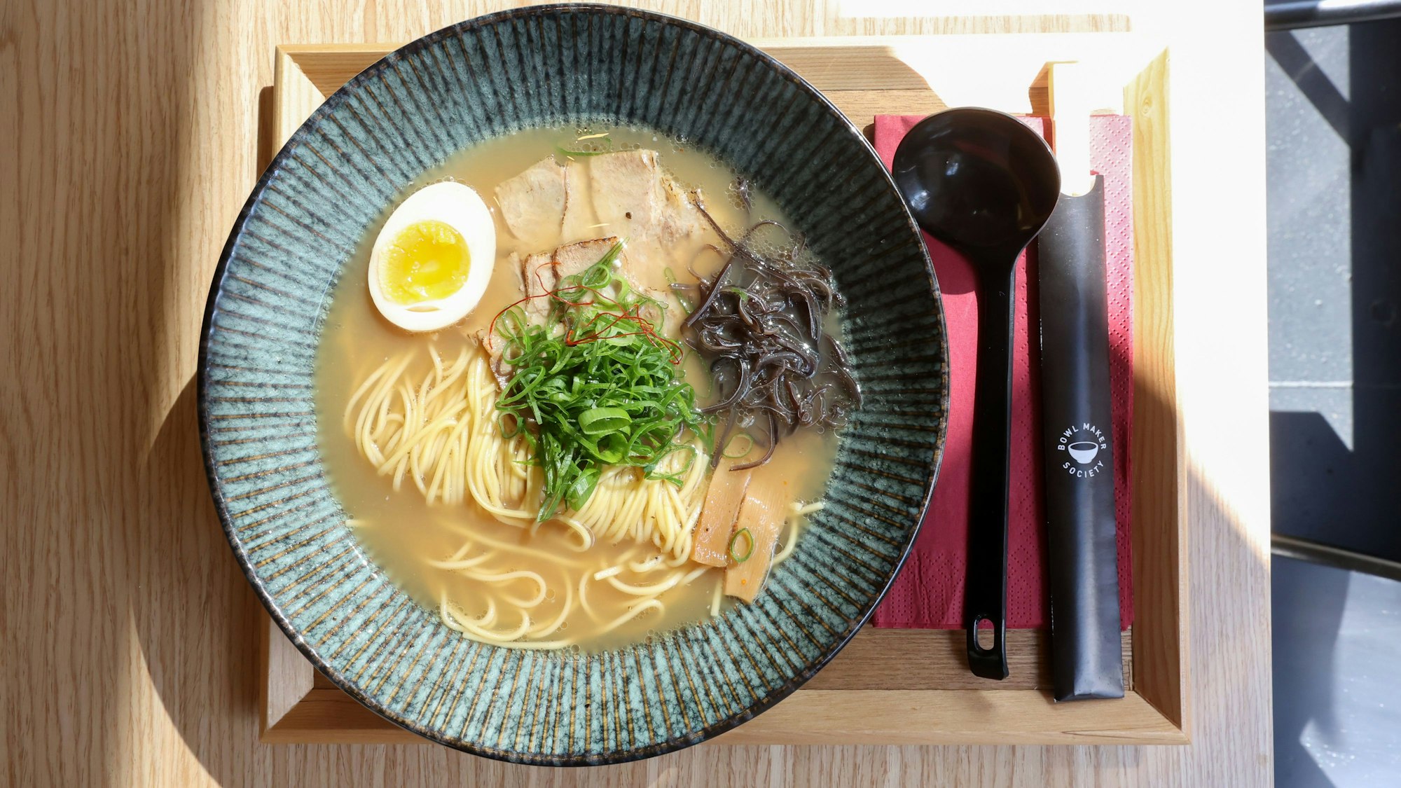 Wir sehen eine Suppenschüssel von oben, daneben Löffel und Stäbchen.