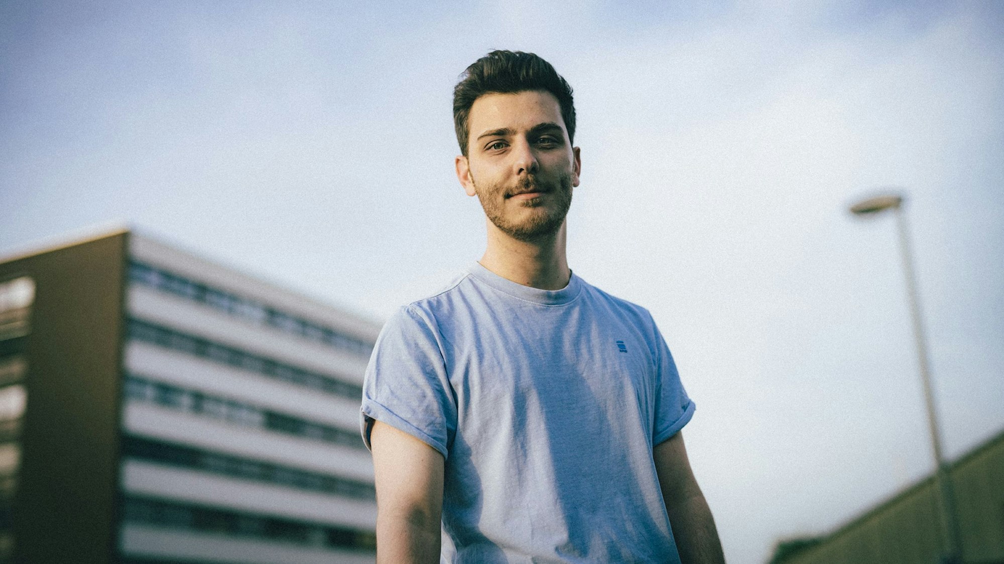 Comedy-Autor, Podcaster und Moderator Tarkan Bagci trägt ein blaues T-Shirt und blickt in die Kamera.