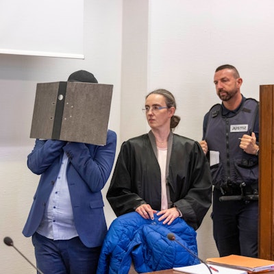 Der Angeklagte kommt vor der Verkündung des Urteils im Prozess wegen sexuellen Missbrauchs an Kindern in den Gerichtssaal des Kölner Landgerichts, während er sein Gesicht hinter einem Aktenordner verbirgt. Seine beiden Rechtsanwälte Jürgen Schüttler (links) und Sybille Weber (rechts) erwarten den Angeklagten im Gerichtssaal.