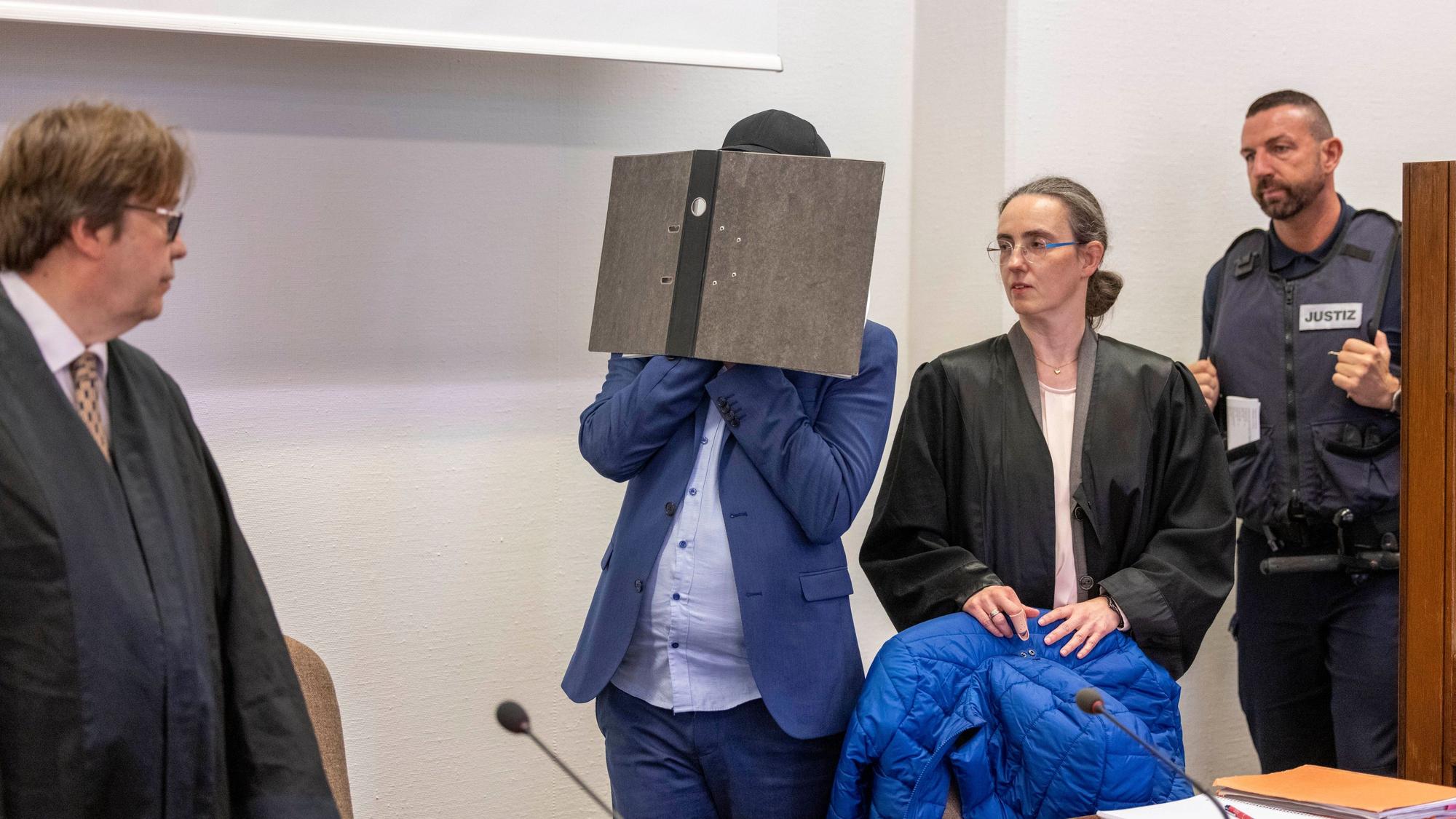 Der Angeklagte kommt vor der Verkündung des Urteils im Prozess wegen sexuellen Missbrauchs an Kindern in den Gerichtssaal des Kölner Landgerichts, während er sein Gesicht hinter einem Aktenordner verbirgt. Seine beiden Rechtsanwälte Jürgen Schüttler (links) und Sybille Weber (rechts) erwarten den Angeklagten im Gerichtssaal.