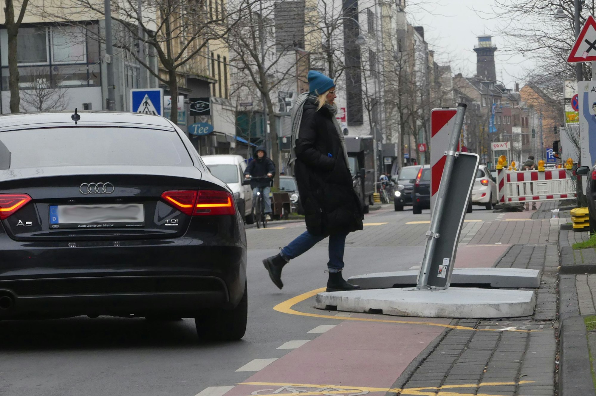 Ein Auto kurvt um ein Fahrbahn-verengendes Element, während eine Fußgängerin die Straße überquert.