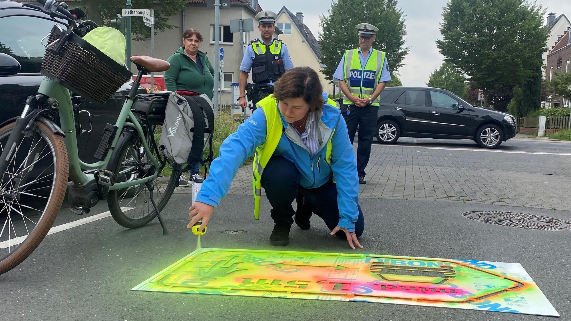 Christiane Jäger, Fachbereichsleiterin für Mobilität und Klimaschutz, sprayt einen signalfarbenen Hinweis auf die Straße.