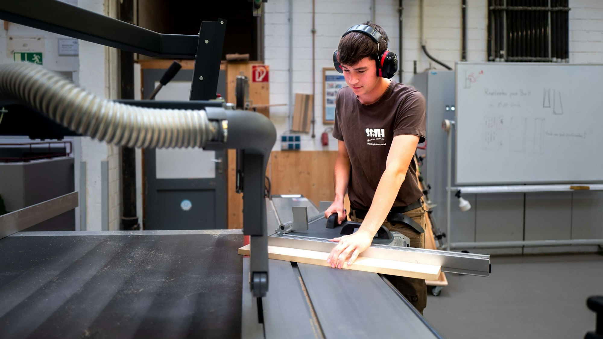 Ein junger Mann steht an einer Säge und bearbeitet ein Brett.