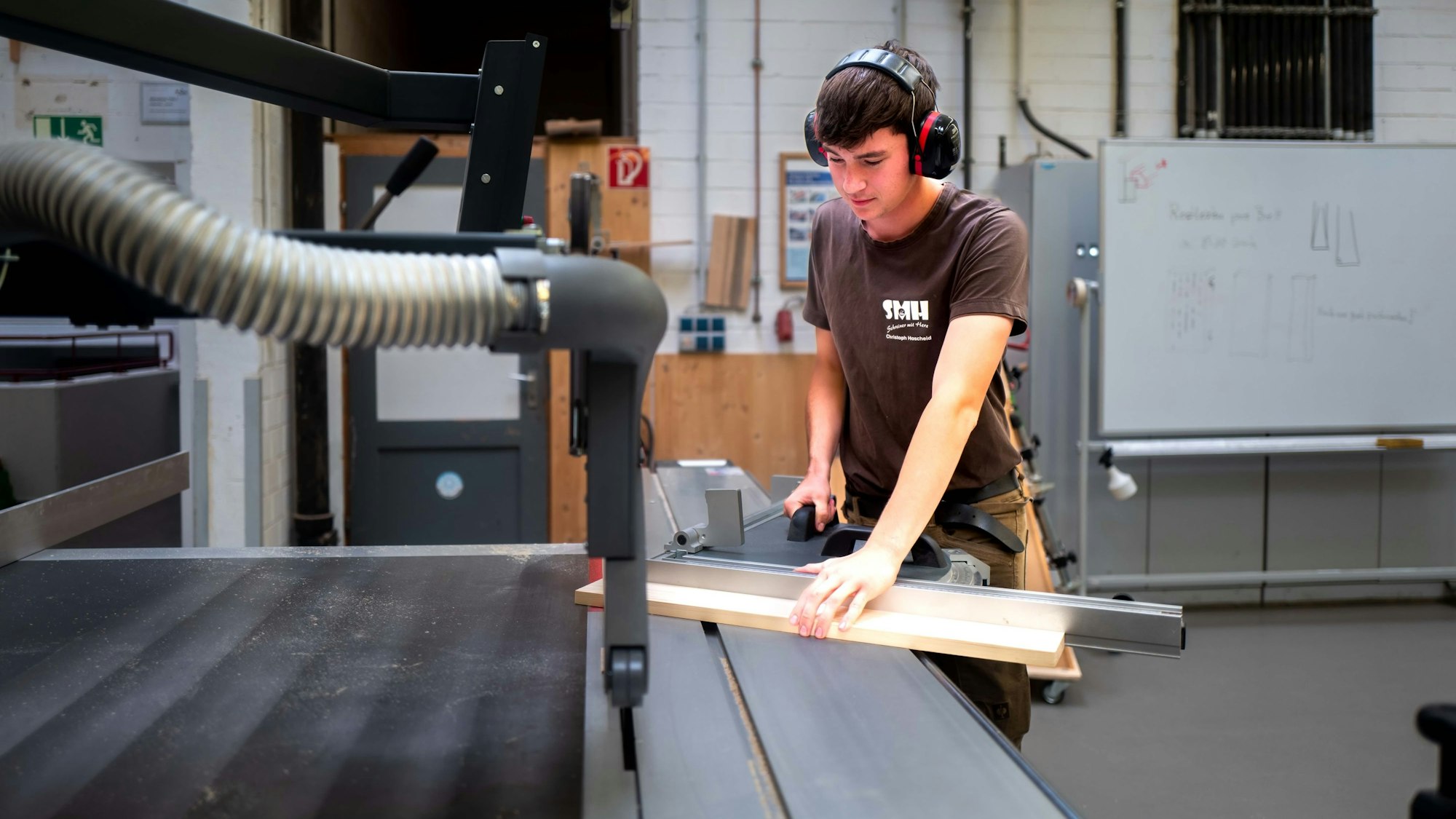 Das Bild zeigt einen Auszubildenden, während er ein Holzbrett in die Kreissäge schiebt.