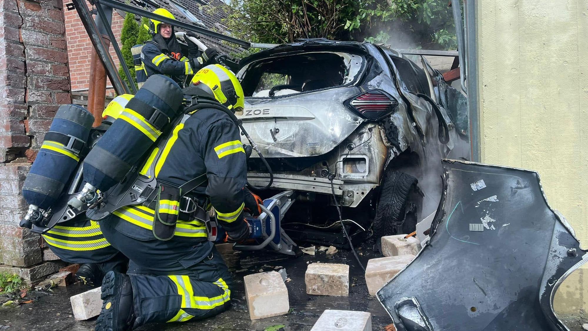 Einsatz in Neuss: Feuerwehrleute löschen und bearbeiten das E-Autowrack, das nach einem Akkudefekt in einer Garage am Sonntag, 27. August, explodiert ist.