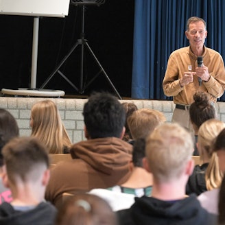 Der Autor Lutz van Dijk steht mit einem Mikrofon in der Hand vor Schülerinnen und Schülern.
