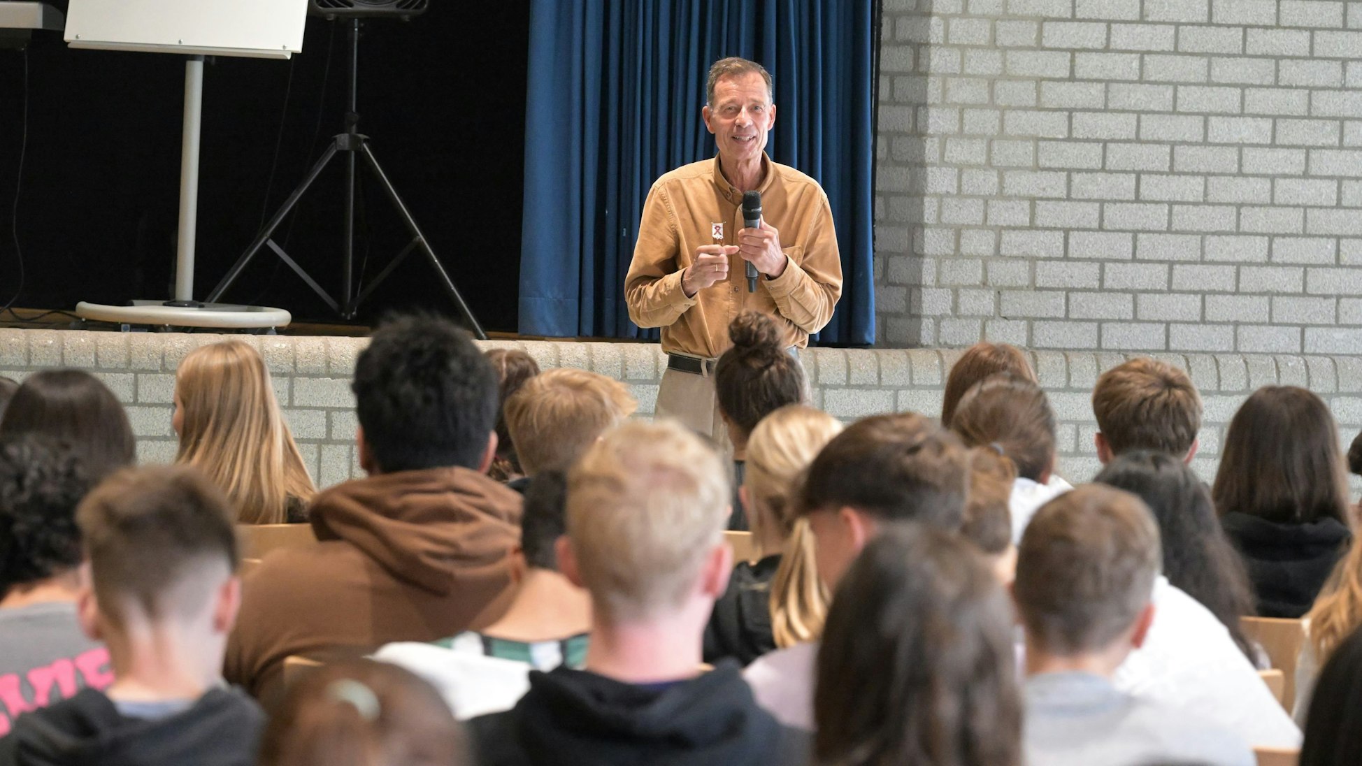 Der Autor Lutz van Dijk steht mit einem Mikrofon in der Hand vor Schülerinnen und Schülern.