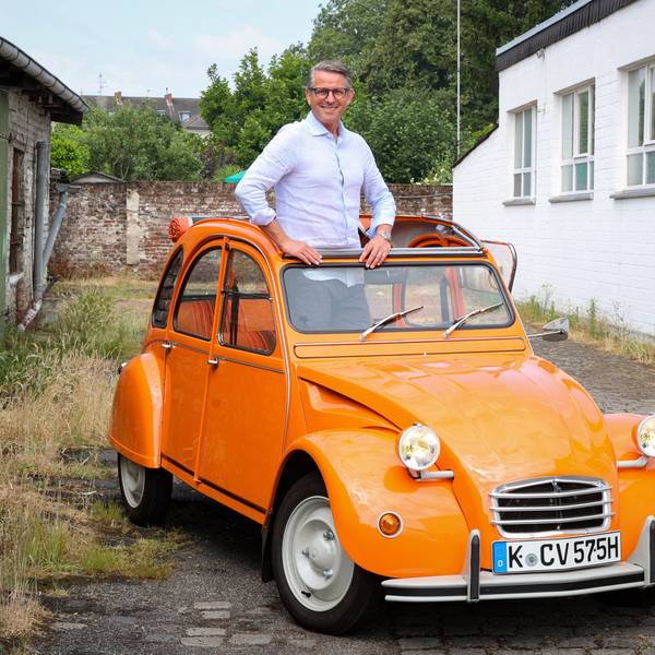 Mann mittleren Alters mit Hemd und Brille, der aus dem Verdeck eines orangefarbenen Oldtimers schaut