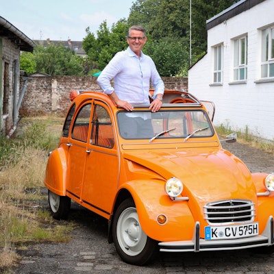 Mann mittleren Alters mit Hemd und Brille, der aus dem Verdeck eines orangefarbenen Oldtimers schaut