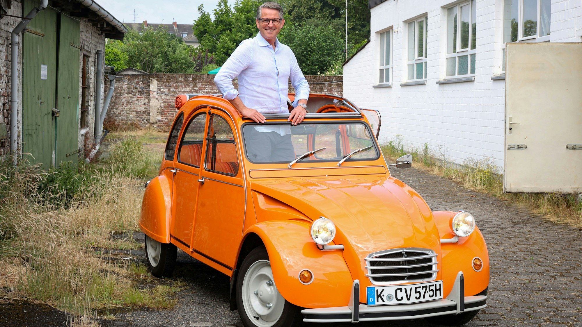 Mann mittleren Alters mit Hemd und Brille, der aus dem Verdeck eines orangefarbenen Oldtimers schaut