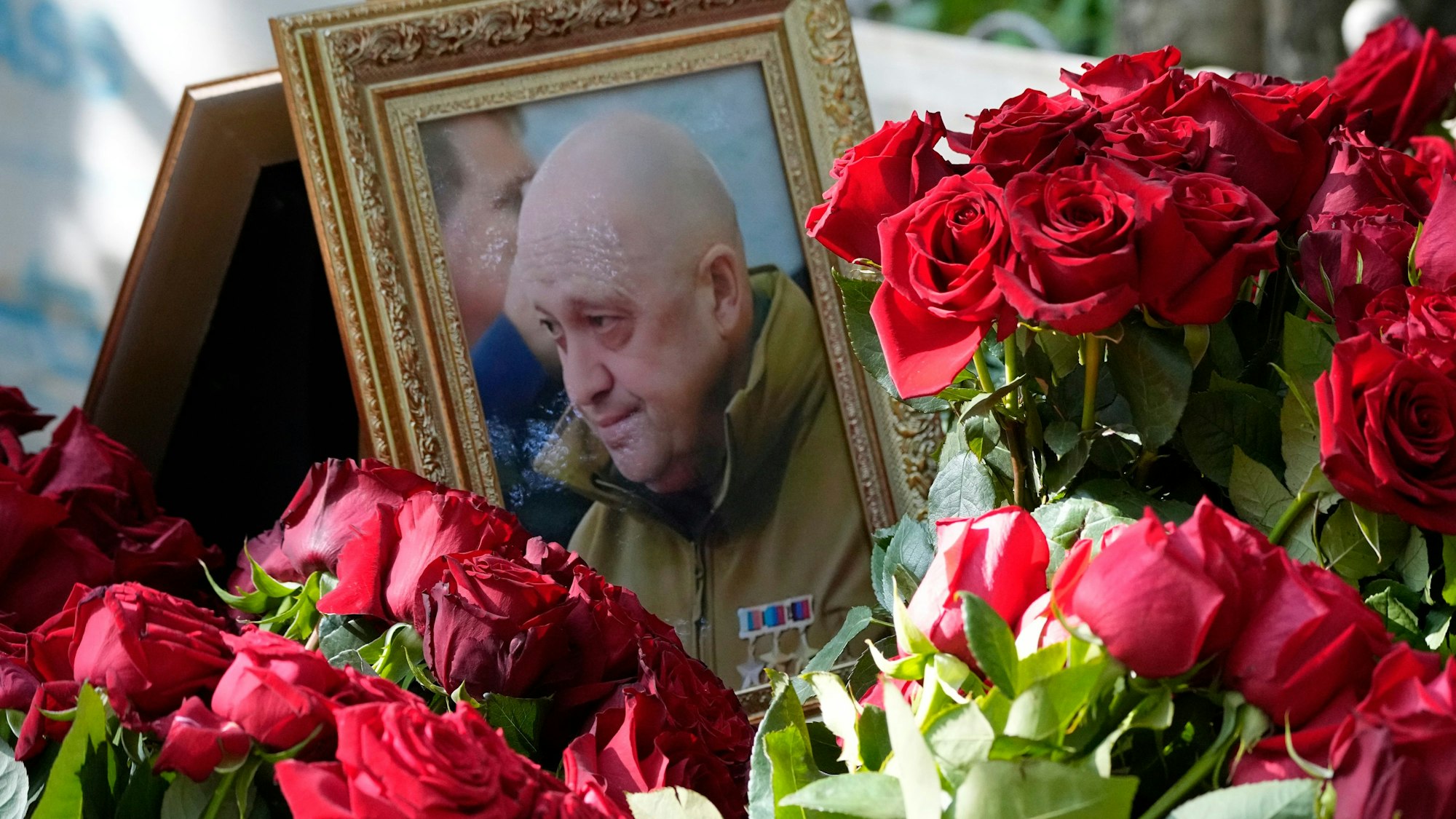 30.08.2023, Russland, St. Petersburg: Ein Porträt des Chefs des Wagner-Konzerns, Jewgeni Prigoschin, der am 23.08.2023 bei einem Flugzeugabsturz ums Leben kam, steht zwischen Blumen auf einem Grab auf dem Friedhof Porochowskoje. Der russische Söldnerführer Jewgeni Prigoschin ist nach Angaben seines Pressedienstes in seiner Heimatstadt St. Petersburg beerdigt worden. Bei einer Trauerfeier im engsten Kreis ohne Öffentlichkeit sei Abschied genommen worden, teilte der Pressedienst des Chefs der Privatarmee Wagner am 29.08.2023 mit. Interessenten, die sich nun auch von dem am 23.08.2023 bei einem Flugzeugabsturz getöteten Geschäftsmann verabschieden wollten, könnten dies auf dem Friedhof Porochowskoje tun, hieß es. Foto: Dmitri Lovetsky/AP/dpa +++ dpa-Bildfunk +++