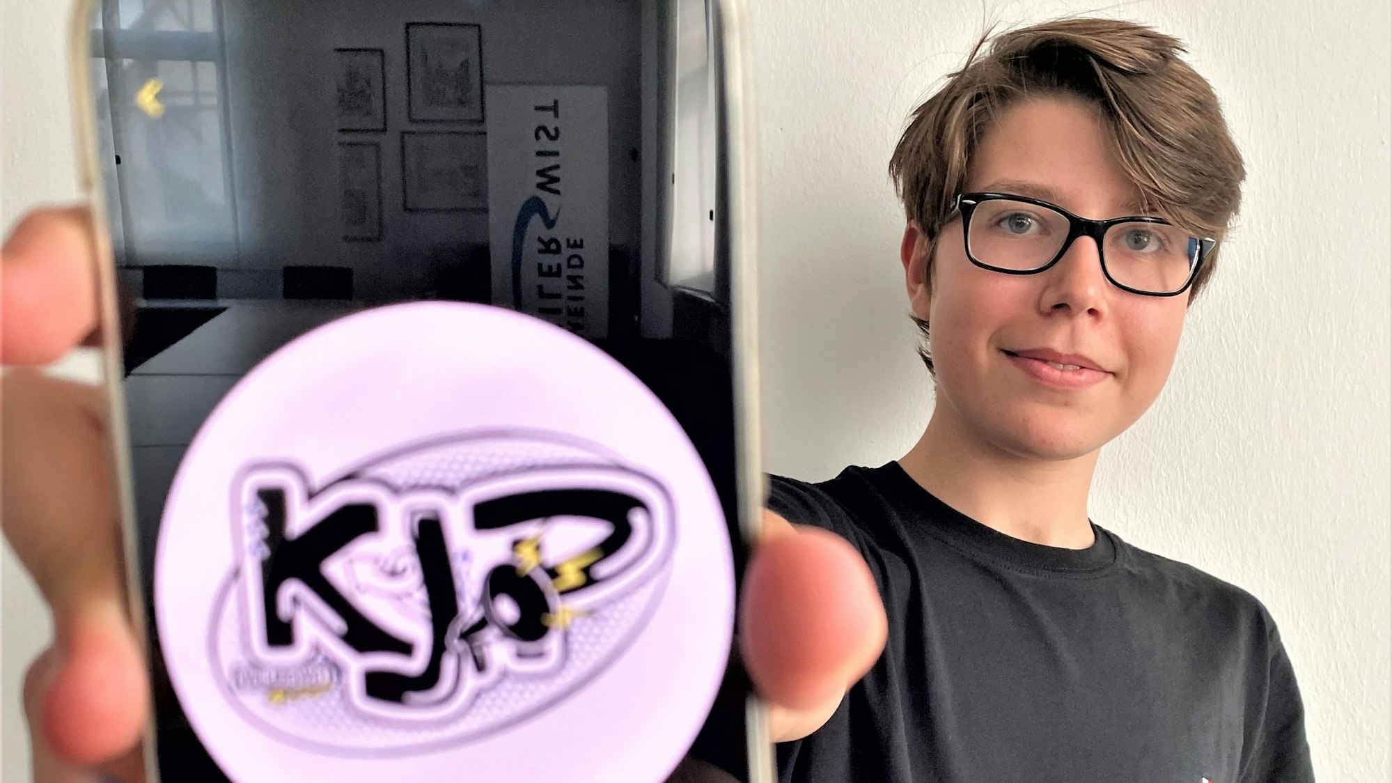Simon Krämer hält ein Handy in die Kamera. Darauf das Emblem des Kinder- und Jugendparlaments.