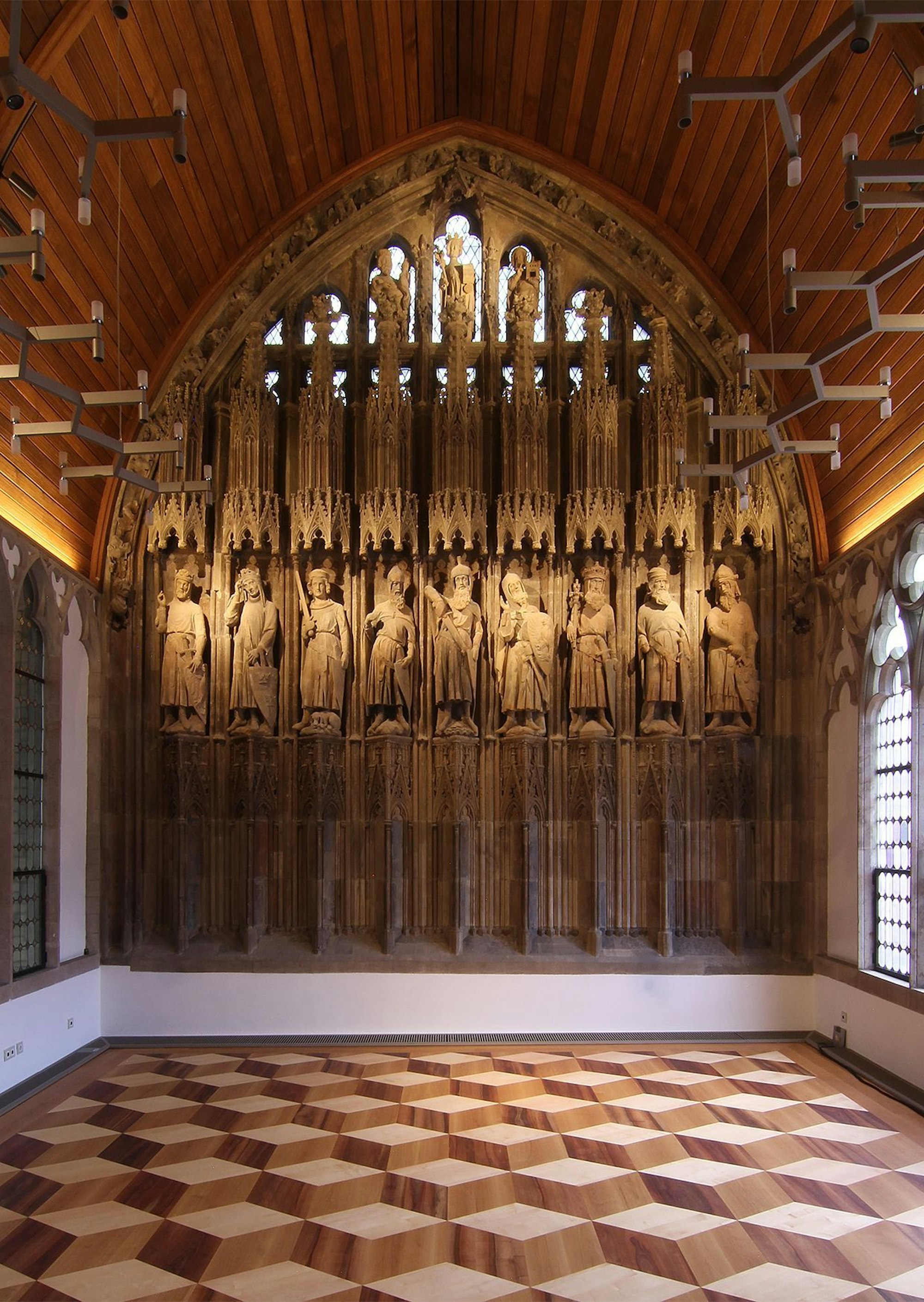 Zu sehen sind die neun Skulpturen, genannt: Gute Helden, und ein brauner Parkettboden mit 3D-Effekt.